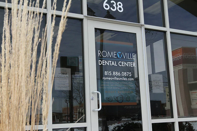 Exterior of Romeoville Dental Center building with entrance signage detailing office contact information and policies.