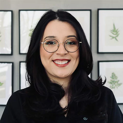 Headshot of Yesenia of Romeoville Dental Center wearing a black scrubs with paintings at the background.