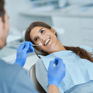 A female patient smiling in a patient chair while a hygienist is holding dental tools at her side